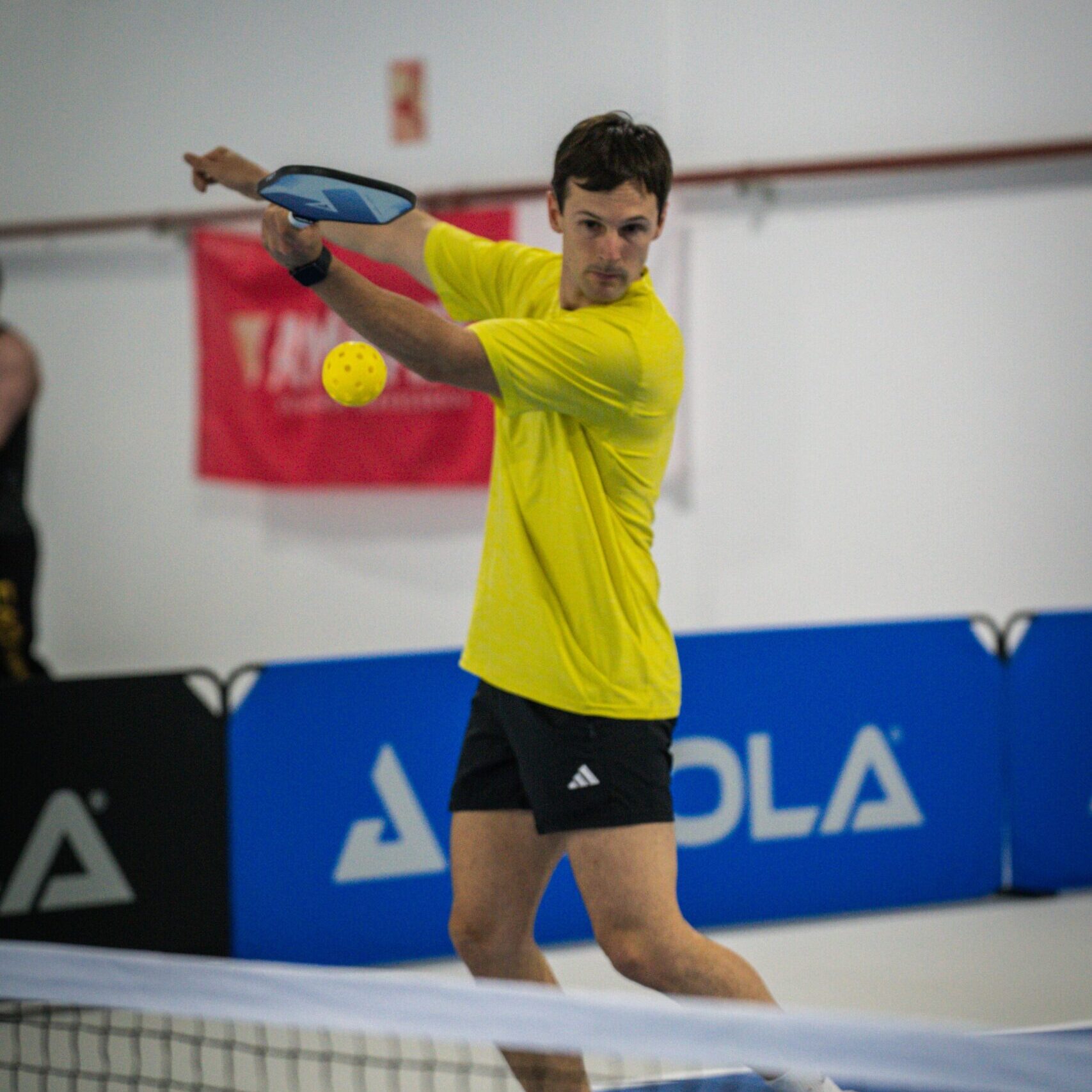 En la imagen se ve un jugador vestida de amarillo, muy concentrado, durante una clase de pickleball en zaragoza